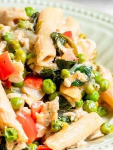 A plate of penne pasta mixed with peas, diced red peppers, spinach, and chunks of chicken, served on a green plate.
