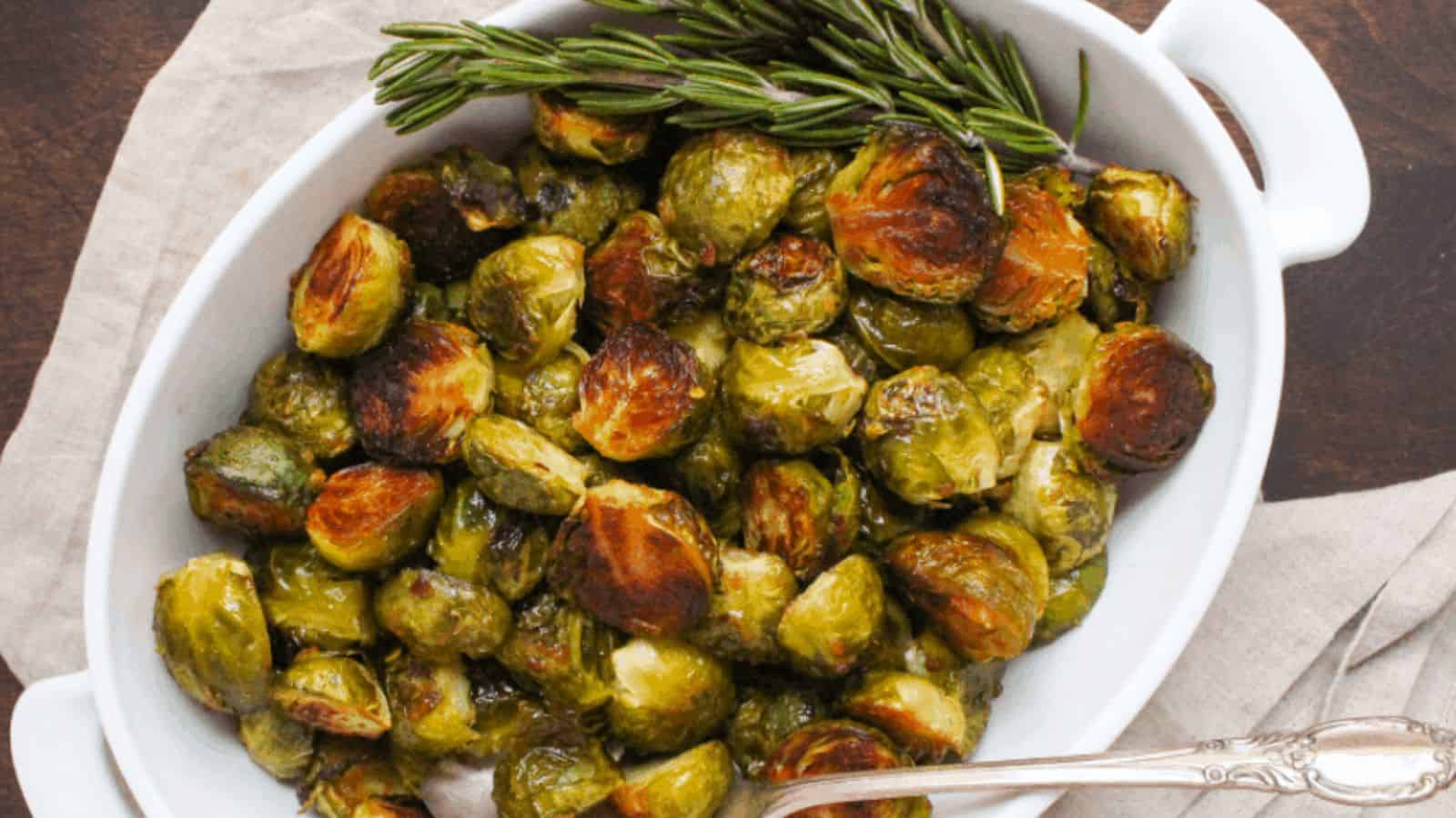 A white serving dish filled with roasted brussels sprouts and fresh rosemary.