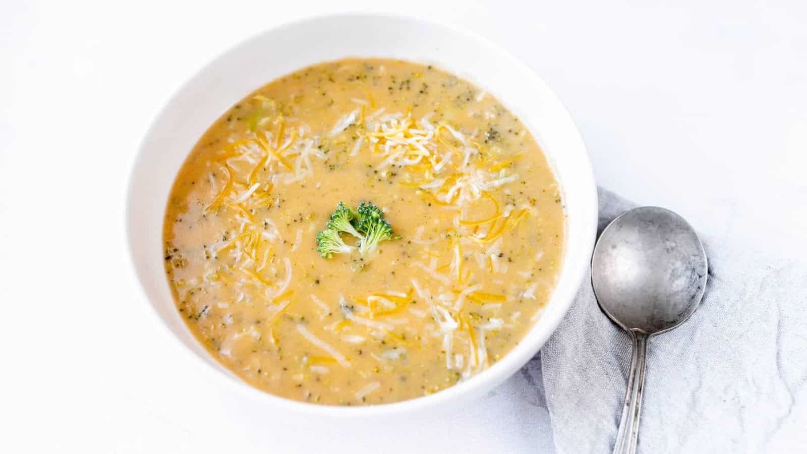 A creamy bowl of Instant Pot Broccoli Cheddar Soup topped with melted cheese and a broccoli garnish, served with a silver spoon.