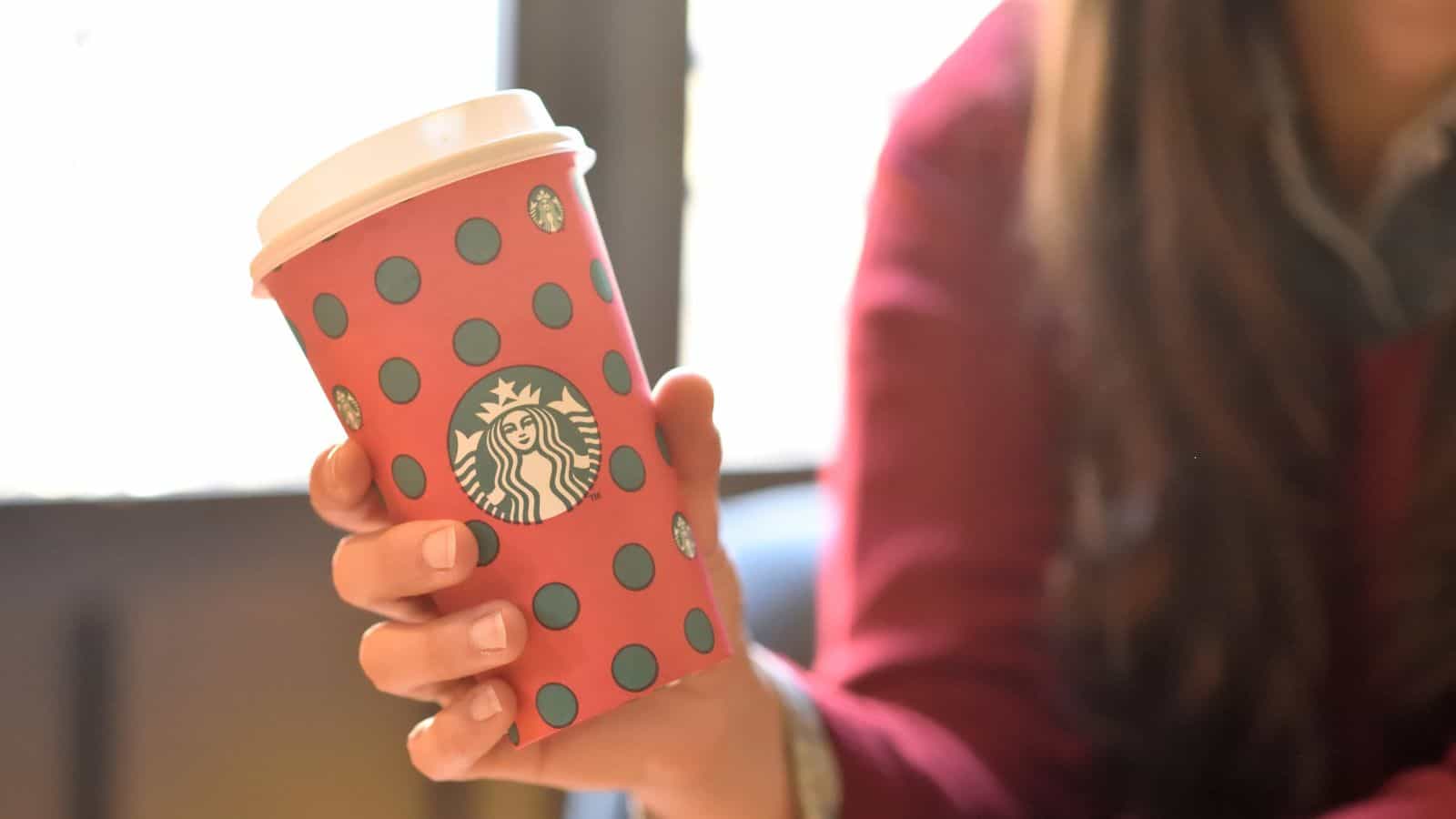 An image of a girl holding a Christmas-themed Starbucks cup.