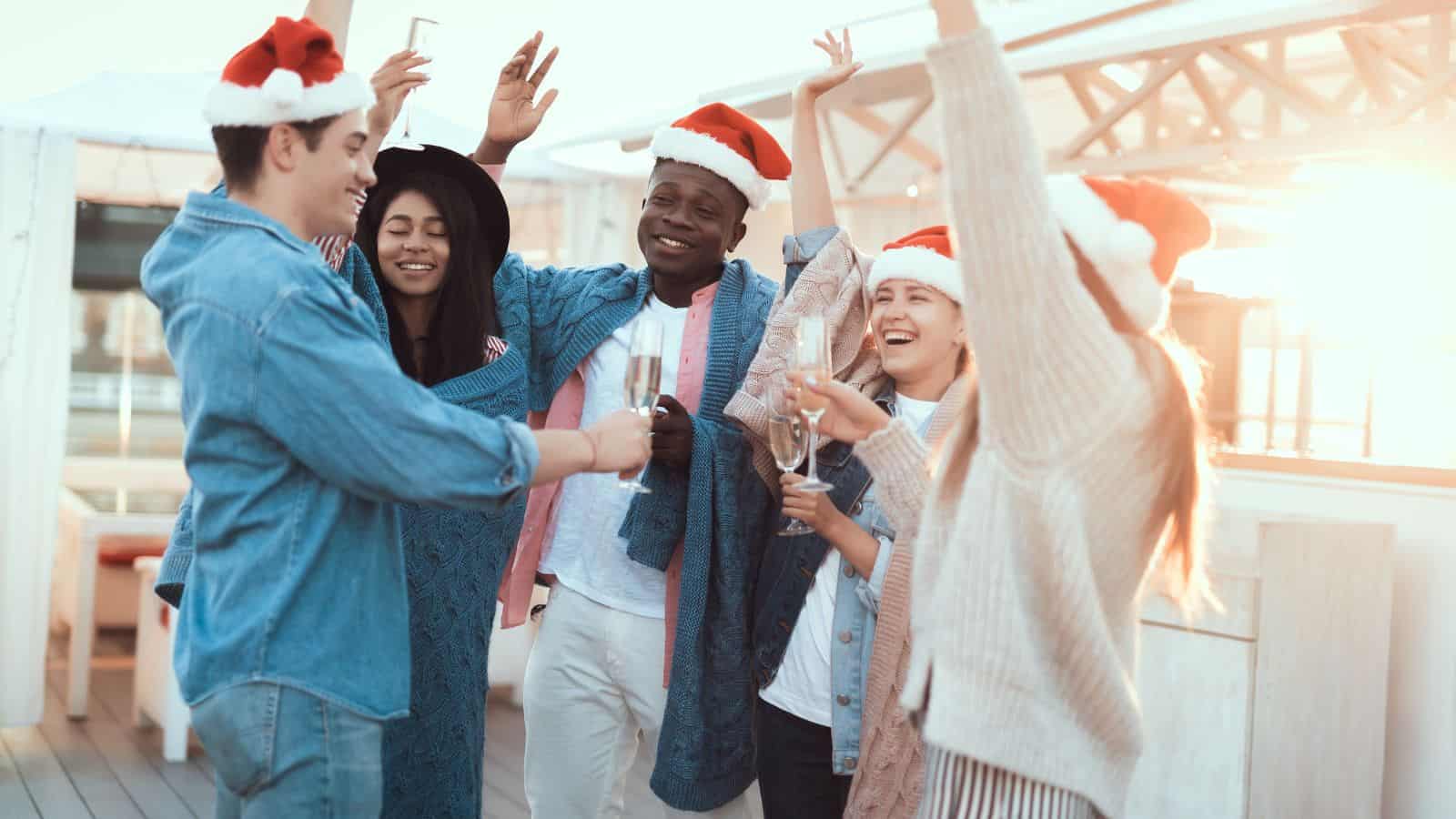 A cheerful group of friends wearing Santa hats celebrating the holidays outdoors with glasses of champagne.