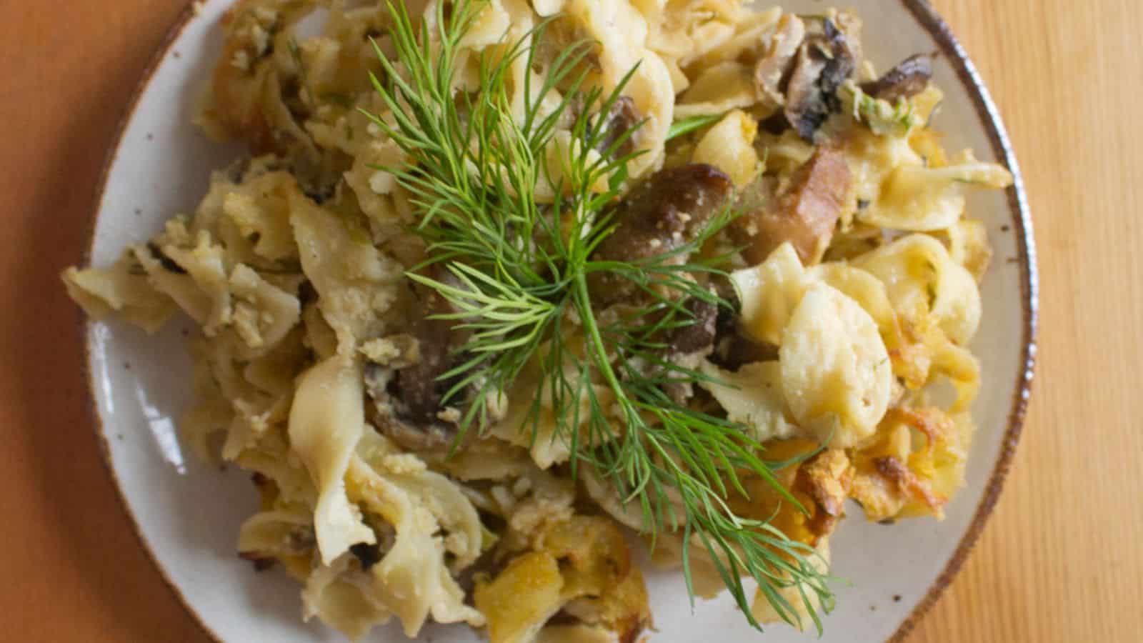 A white dish filled with creamy pasta topped with mushrooms and herbs is placed on a blue and white striped cloth.