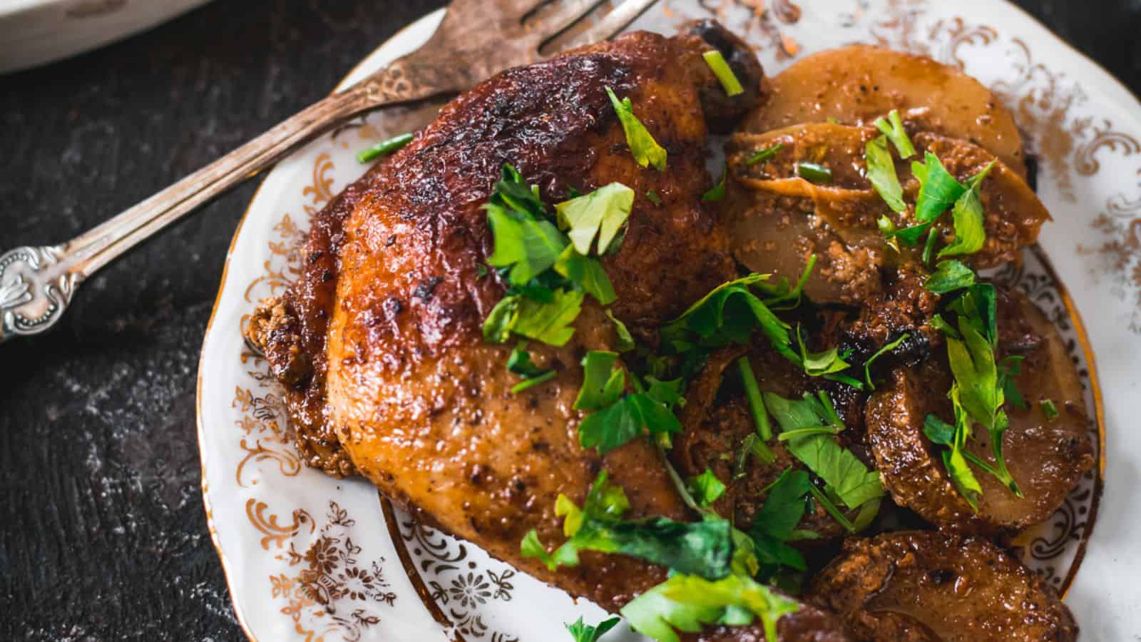 A platter of roasted chicken garnished with fresh parsley, accompanied by saut&eacute;ed mushrooms and potato slices, with a spoon next to the dish. A bowl of creamy white sauce is visible in the background.