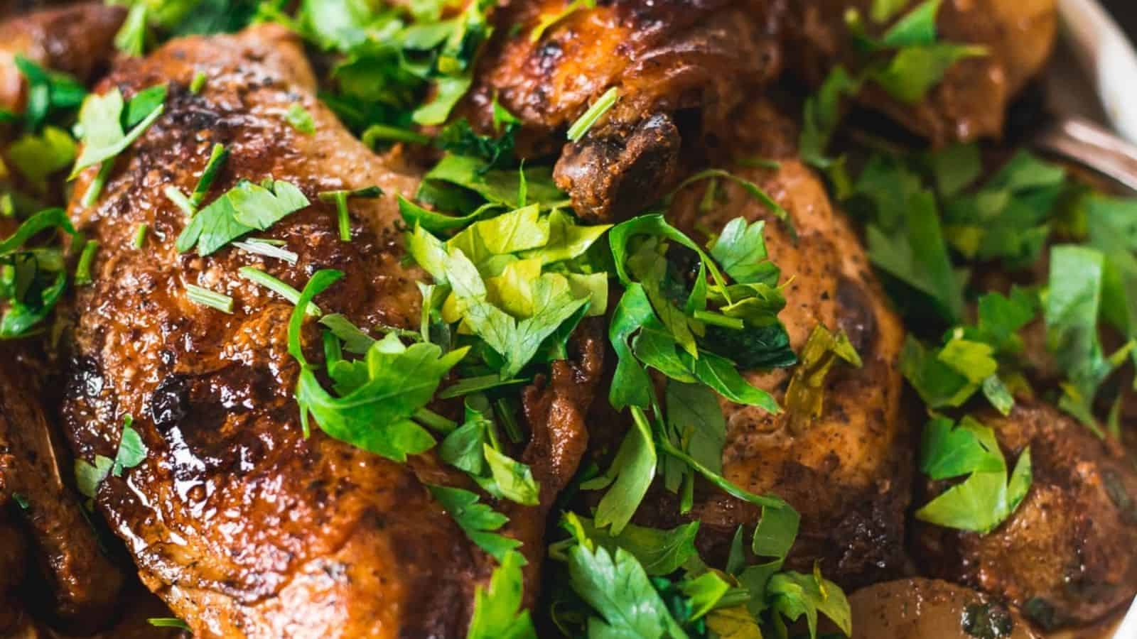 A platter of roasted chicken garnished with fresh parsley, accompanied by sautéed mushrooms and potato slices, with a spoon next to the dish. A bowl of creamy white sauce is visible in the background.