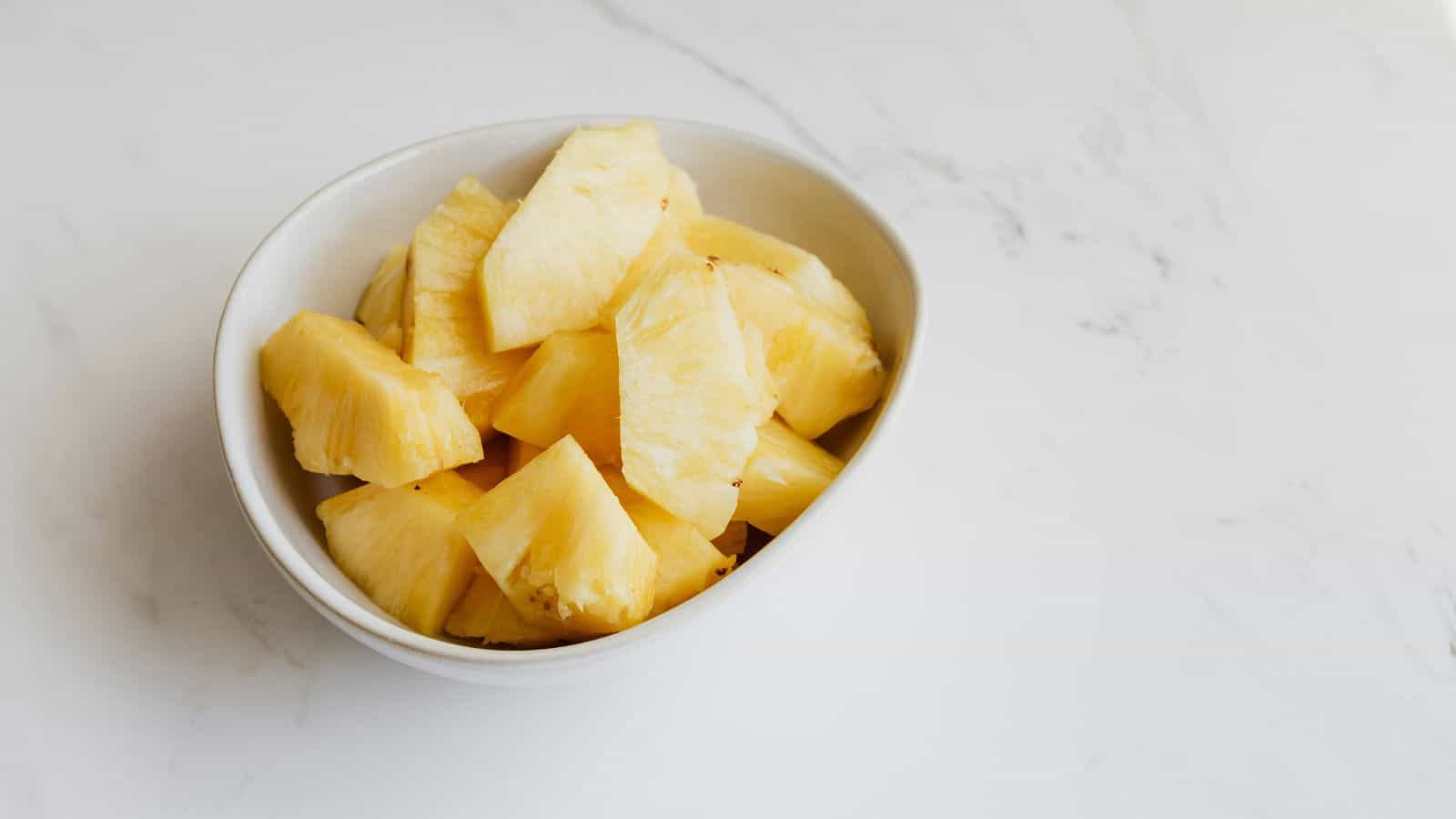 A white bowl filled with slices of fresh pineapple on a marble countertop.