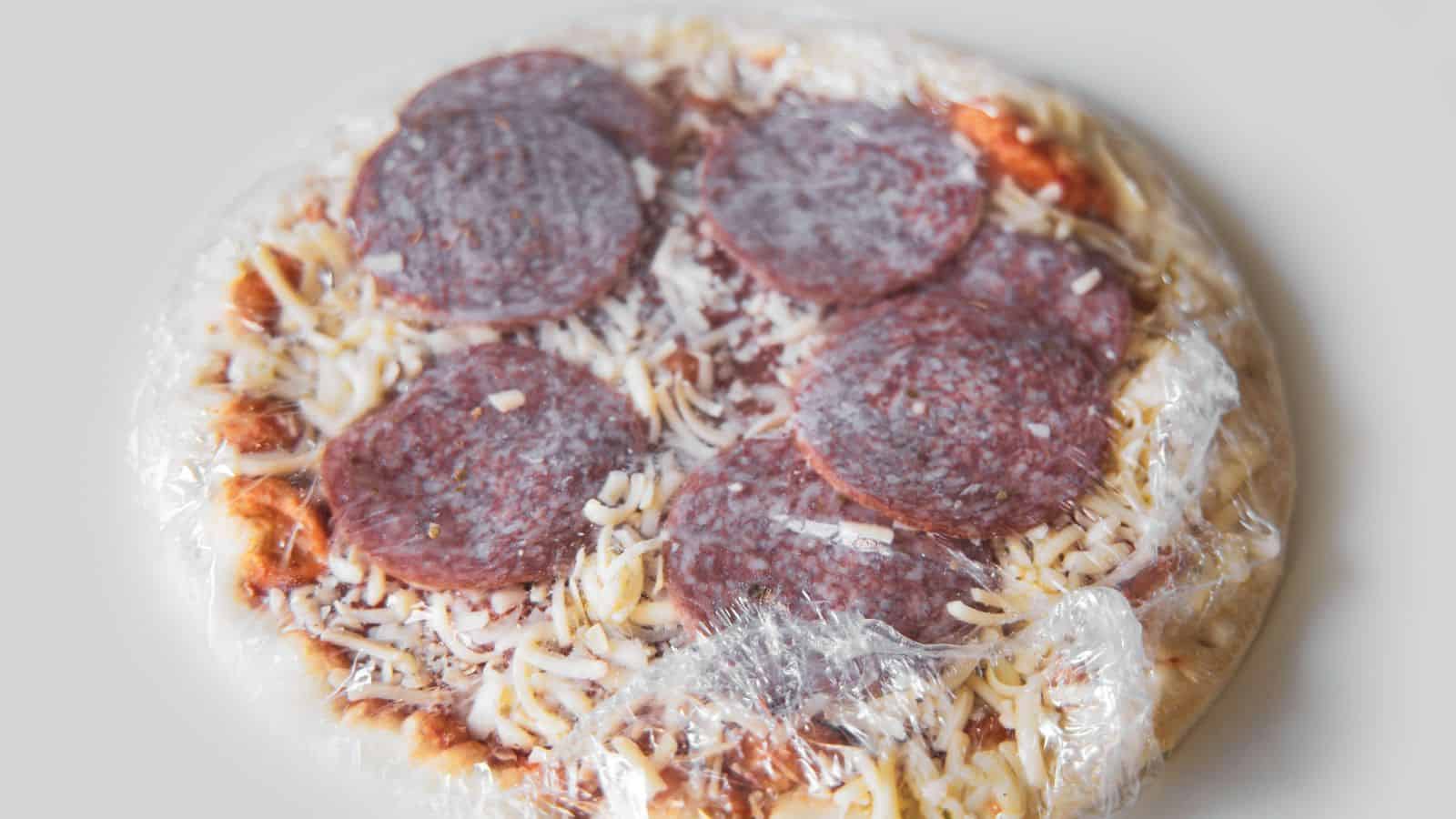 A frozen pepperoni pizza wrapped in clear plastic ready for storage or baking.