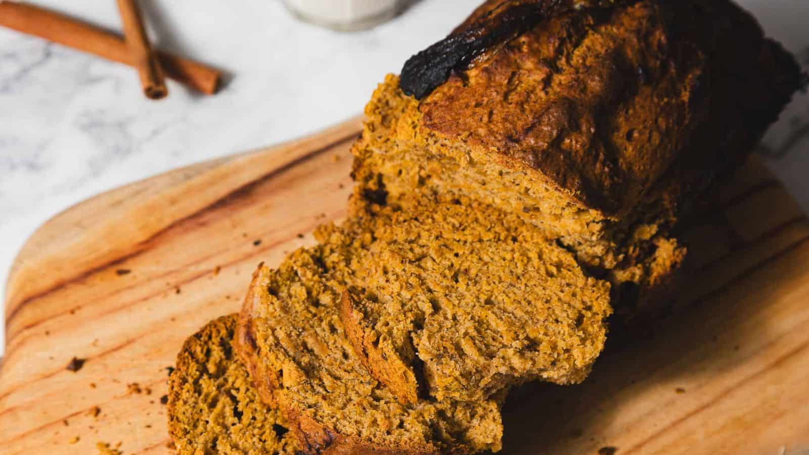 Sliced pumpkin bread on a wooden cutting board next to a glass of milk.