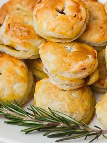 A plate of golden-brown puff pastries stacked on a white dish, garnished with a sprig of rosemary.