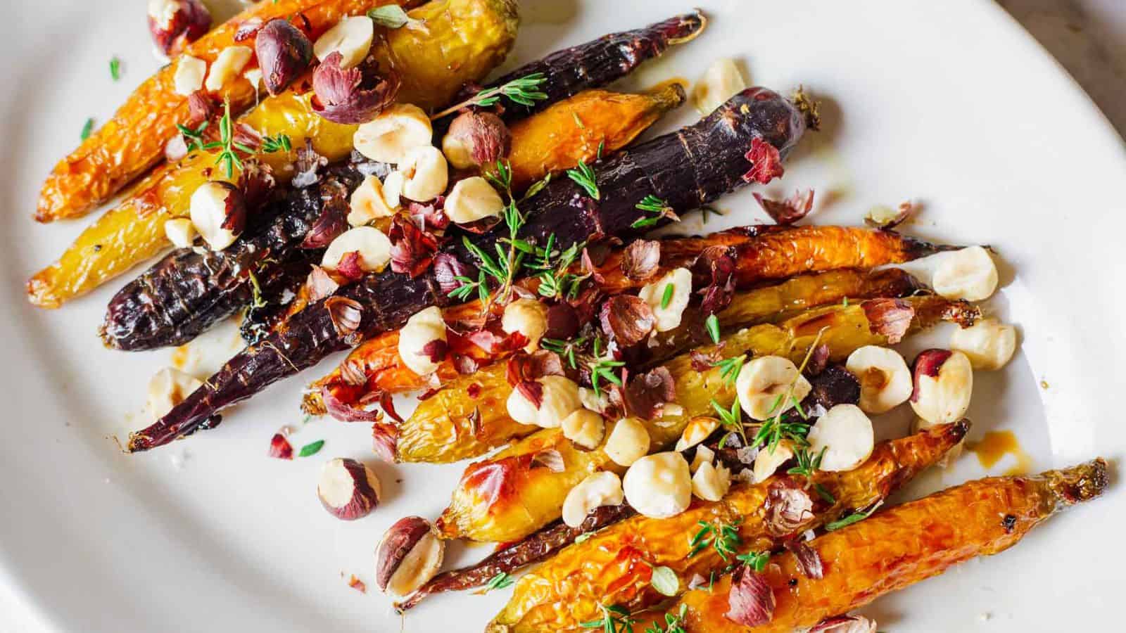 A plate of roasted multicolored carrots topped with chopped hazelnuts and garnished with fresh thyme. The carrots are glazed and appear slightly caramelized, arranged neatly on a white dish.