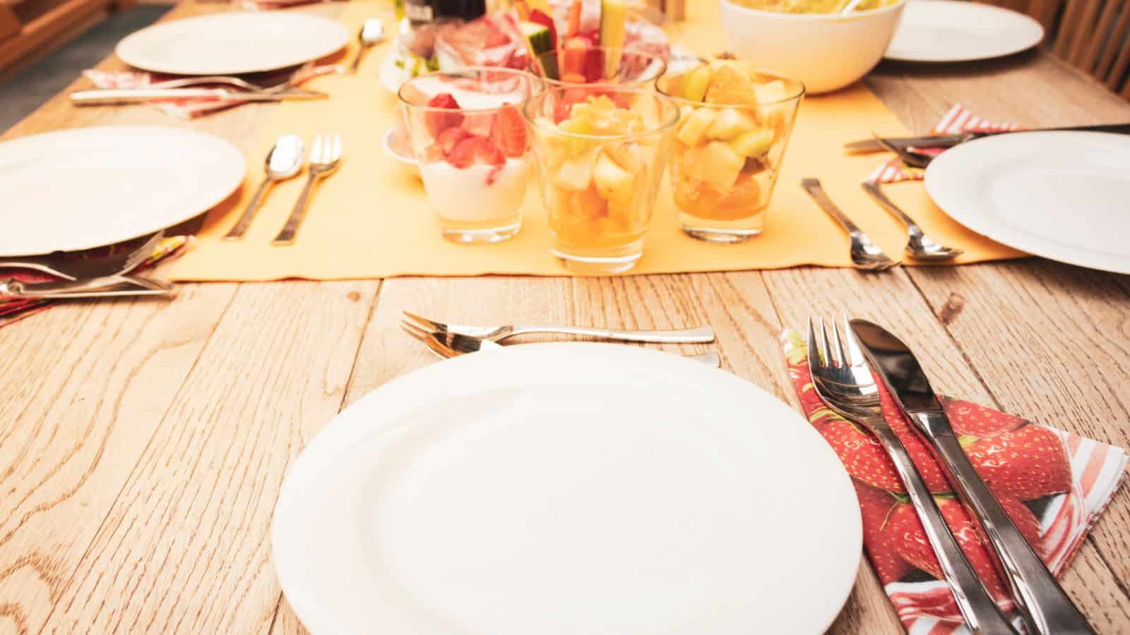 A neatly arranged table with glasses of fruit, yogurt, and cutlery on a wooden surface.