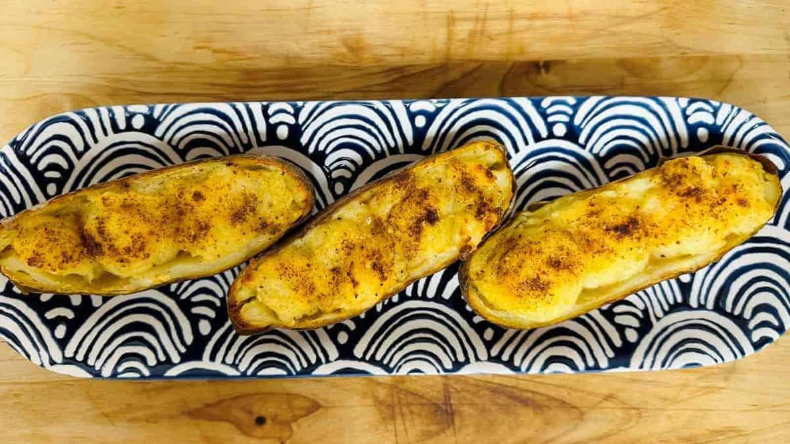 Three baked potatoes on a blue and white plate.