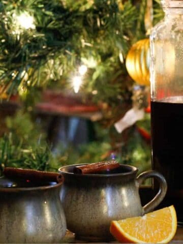 A coffee cup and orange slices next to a glass pitcher.