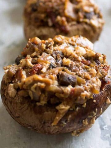 Close-up of stuffed mushrooms on a baking sheet. The mushrooms are topped with a mixture of chopped ingredients, possibly including breadcrumbs, herbs, and vegetables, and appear cooked with a slightly browned surface.