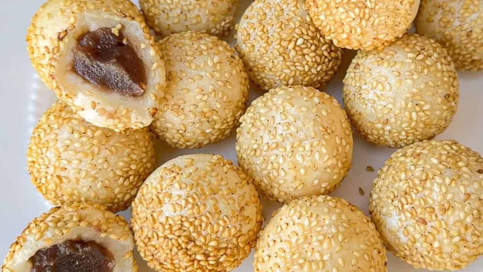 A group of round sesame balls on a white surface. One is cut open, revealing a dark filling inside.