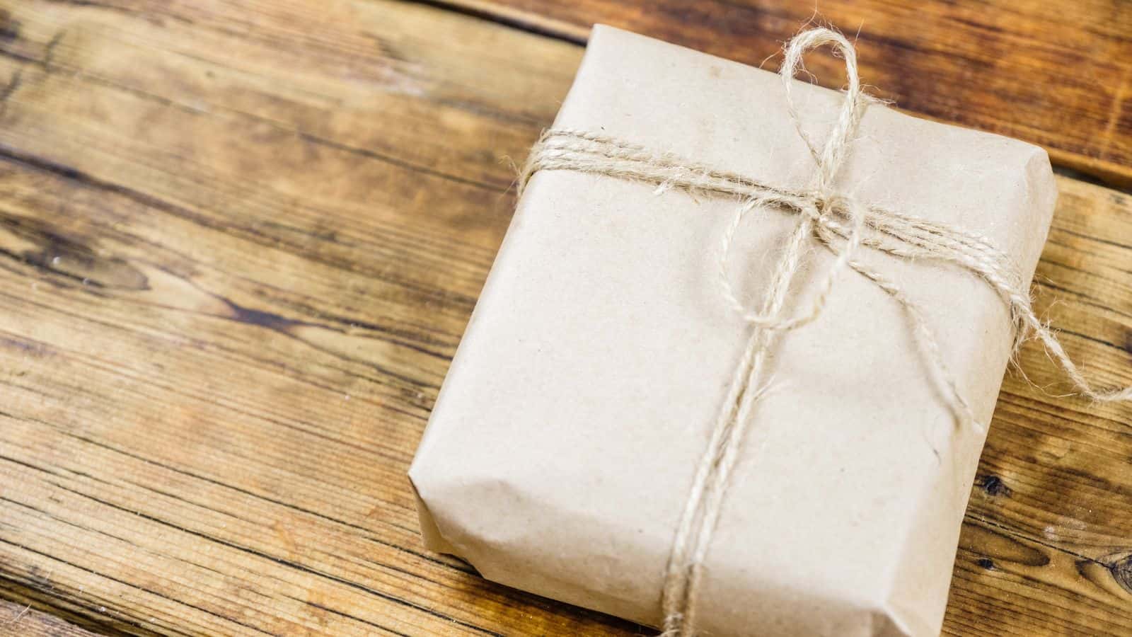 A small package wrapped in plain brown paper and tied with a simple twine is placed on a wooden surface.