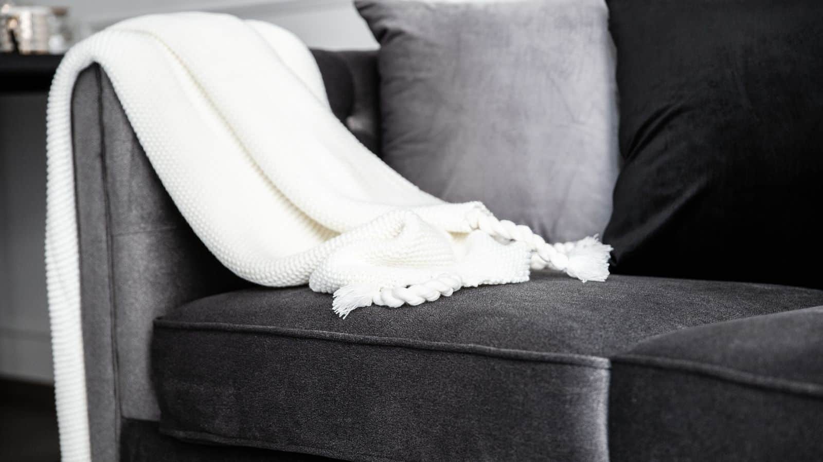 A gray sofa with a white knitted blanket draped over the armrest. The sofa has gray and black cushions, creating a cozy seating arrangement.