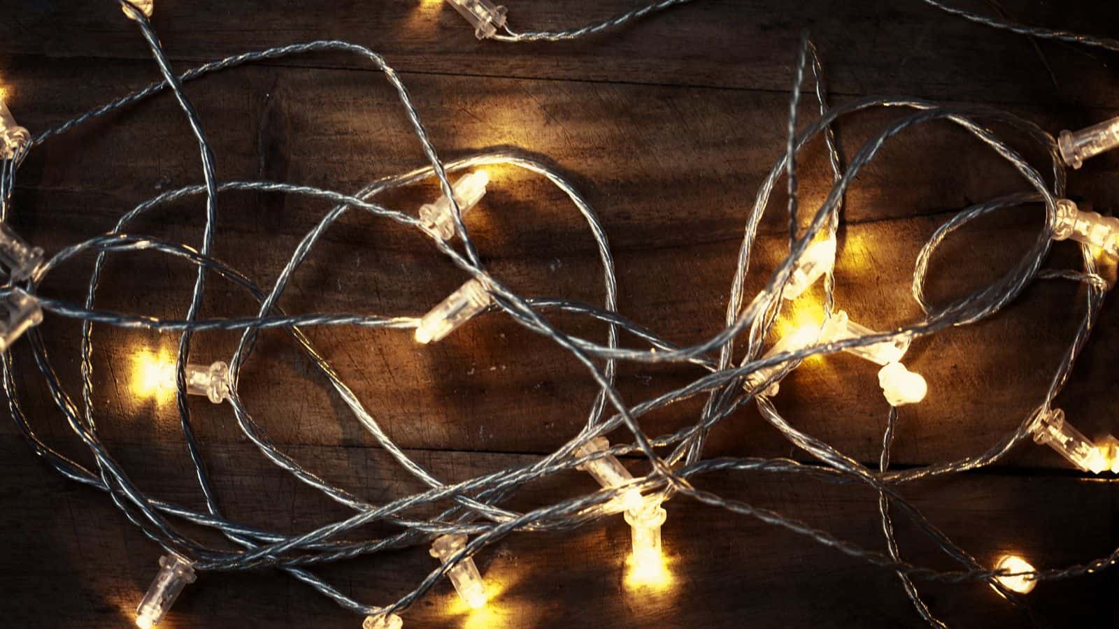 A tangled string of warm white fairy lights is spread out on a dark wooden surface. The lights are turned on, casting a gentle glow.