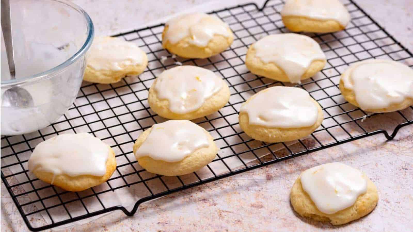 Lemon ricotta cookies on rack with icing bowl.