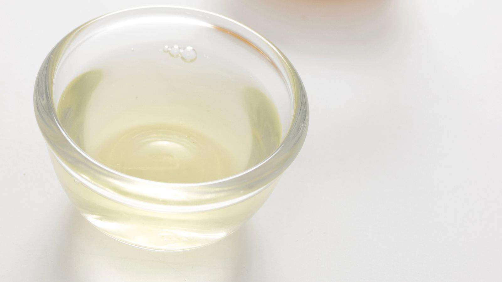 A small, clear glass bowl containing a light yellow liquid is placed on a white surface.