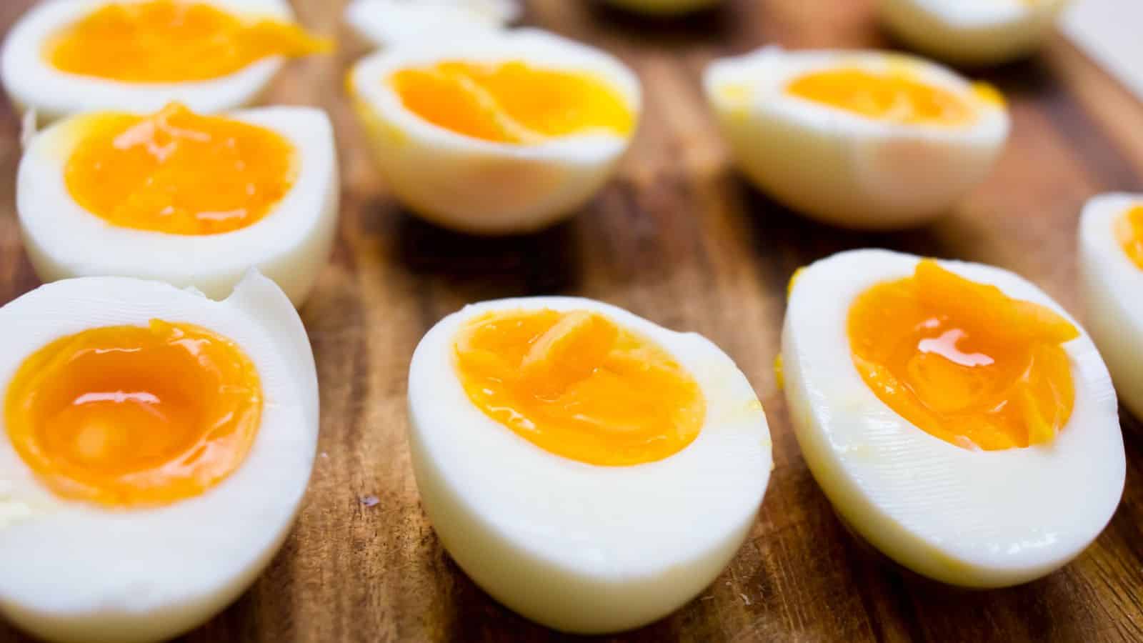 Close-up of several soft-boiled eggs cut in half, showcasing bright yellow yolks and firm whites, arranged on a wooden surface.