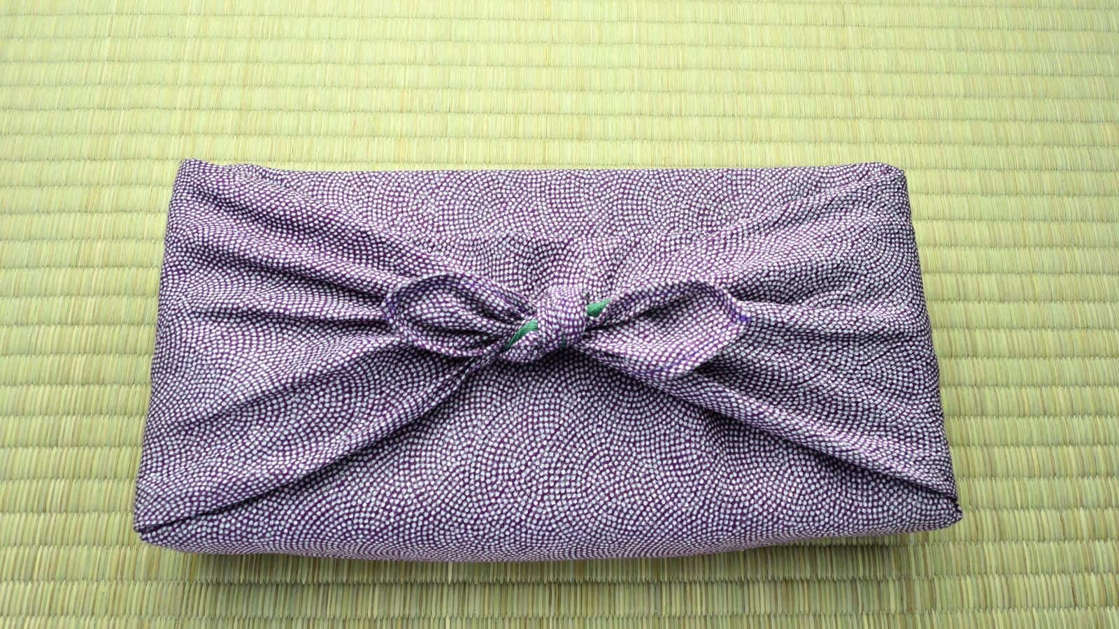 A cloth-wrapped package on a tatami mat. The fabric is purple with a dotted pattern and tied in a bow.