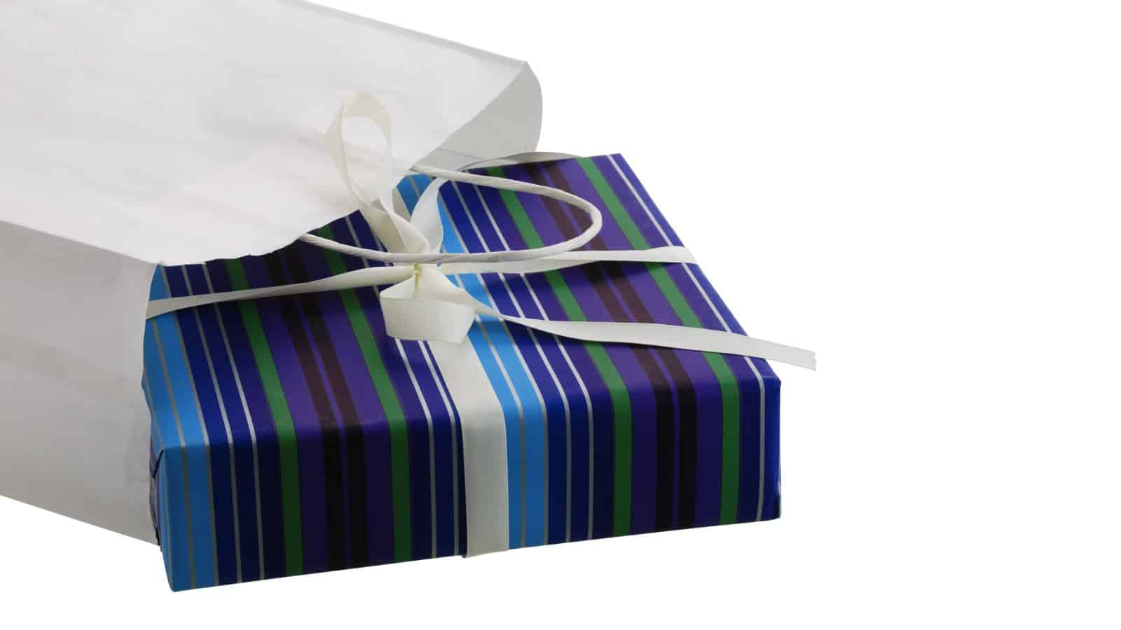 A white shopping bag partially reveals a rectangular gift box wrapped in blue, green, and purple striped paper. The box is adorned with a white ribbon bow.