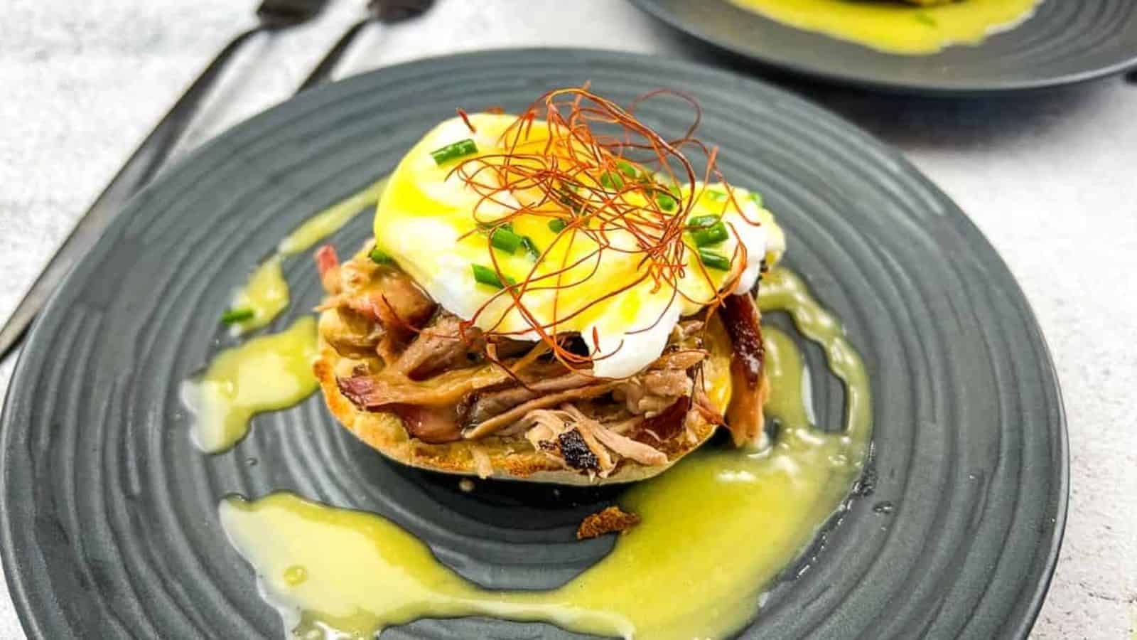 Two pulled pork eggs benedict on a plate with sauce.