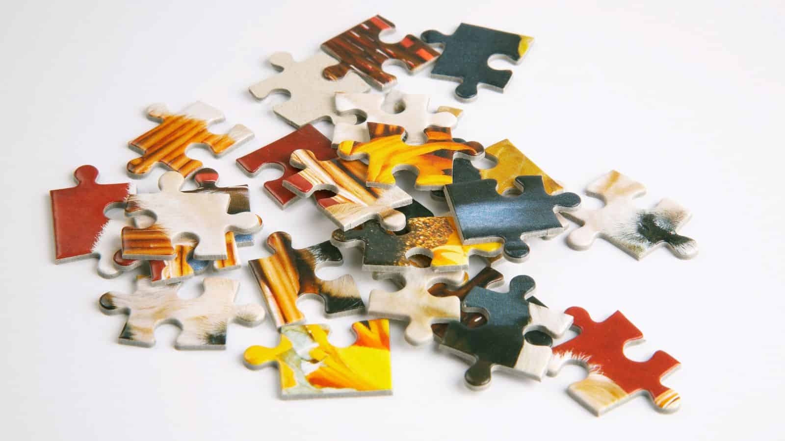 A scattered pile of colorful jigsaw puzzle pieces on a white surface. The pieces display various colors and patterns, but do not form a complete image.
