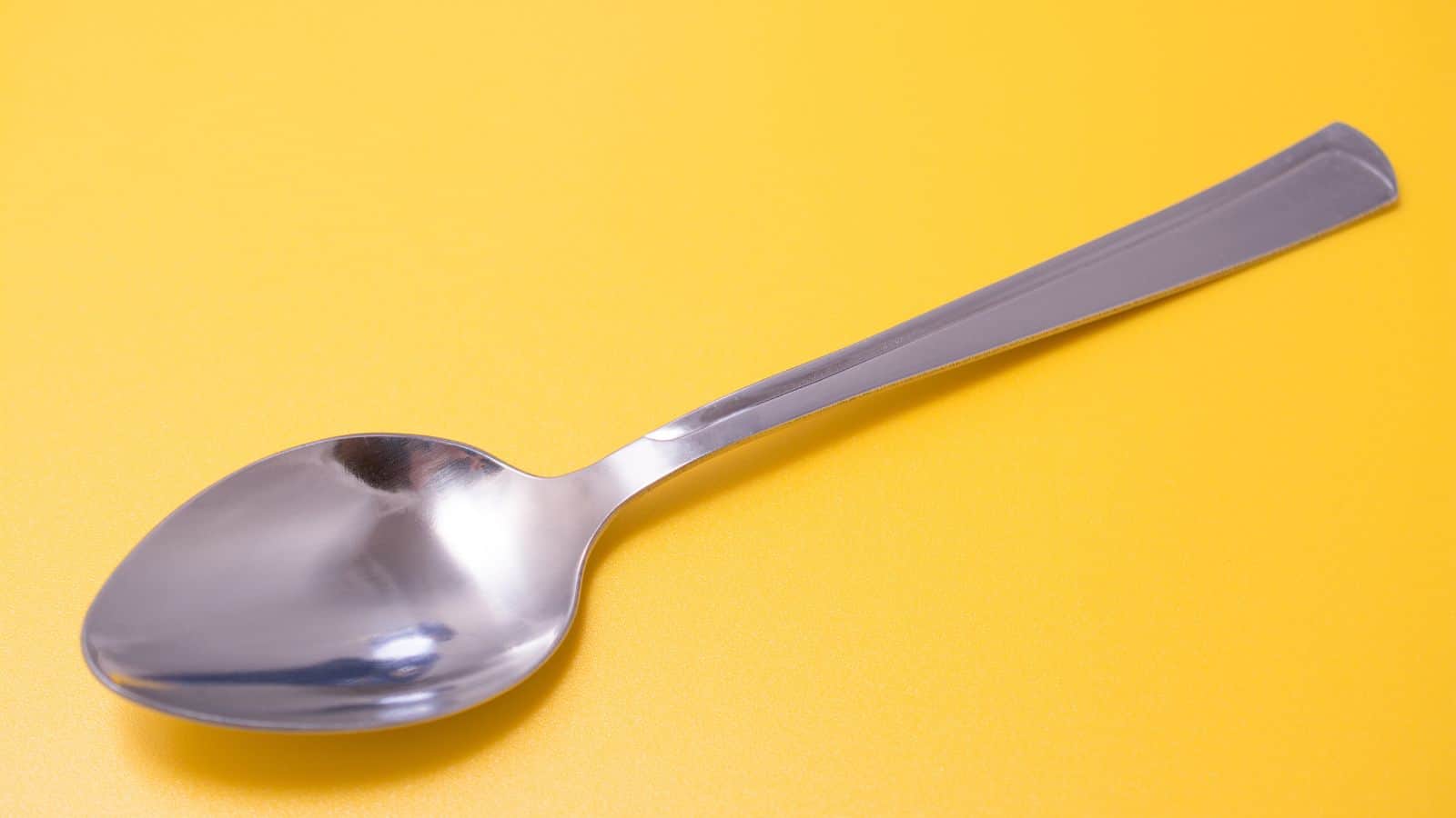 A silver spoon resting on a yellow surface.