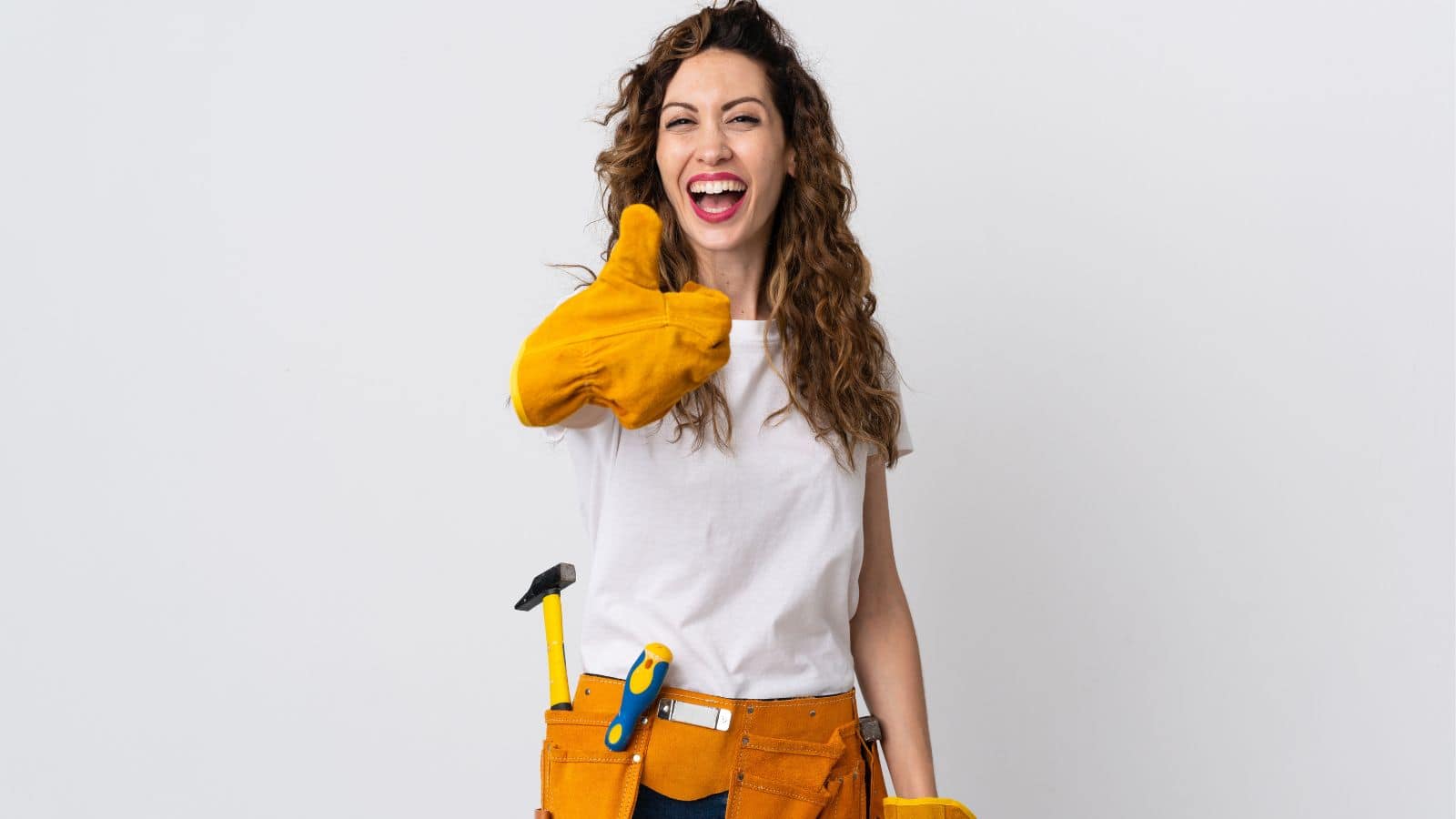 A woman wearing a white T-shirt and a tool belt gives a thumbs-up gesture. She is smiling and wearing yellow work gloves. There are tools like a hammer and a screwdriver in her belt. The background is plain white.