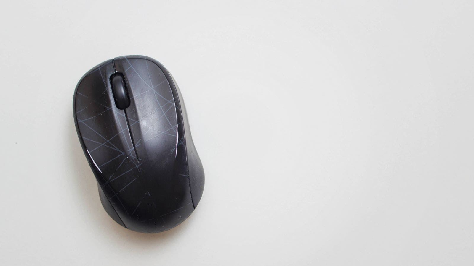 A black computer mouse with visible wear and light scratches on its surface is placed on a plain white background. The mouse is angled slightly to the left, showing the scroll wheel and part of the top surface.