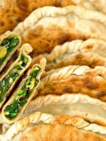 A basket filled with several golden-brown pastries, some halved to show a green vegetable filling. The pastries are arranged neatly, highlighting their crimped edges and textured surface.