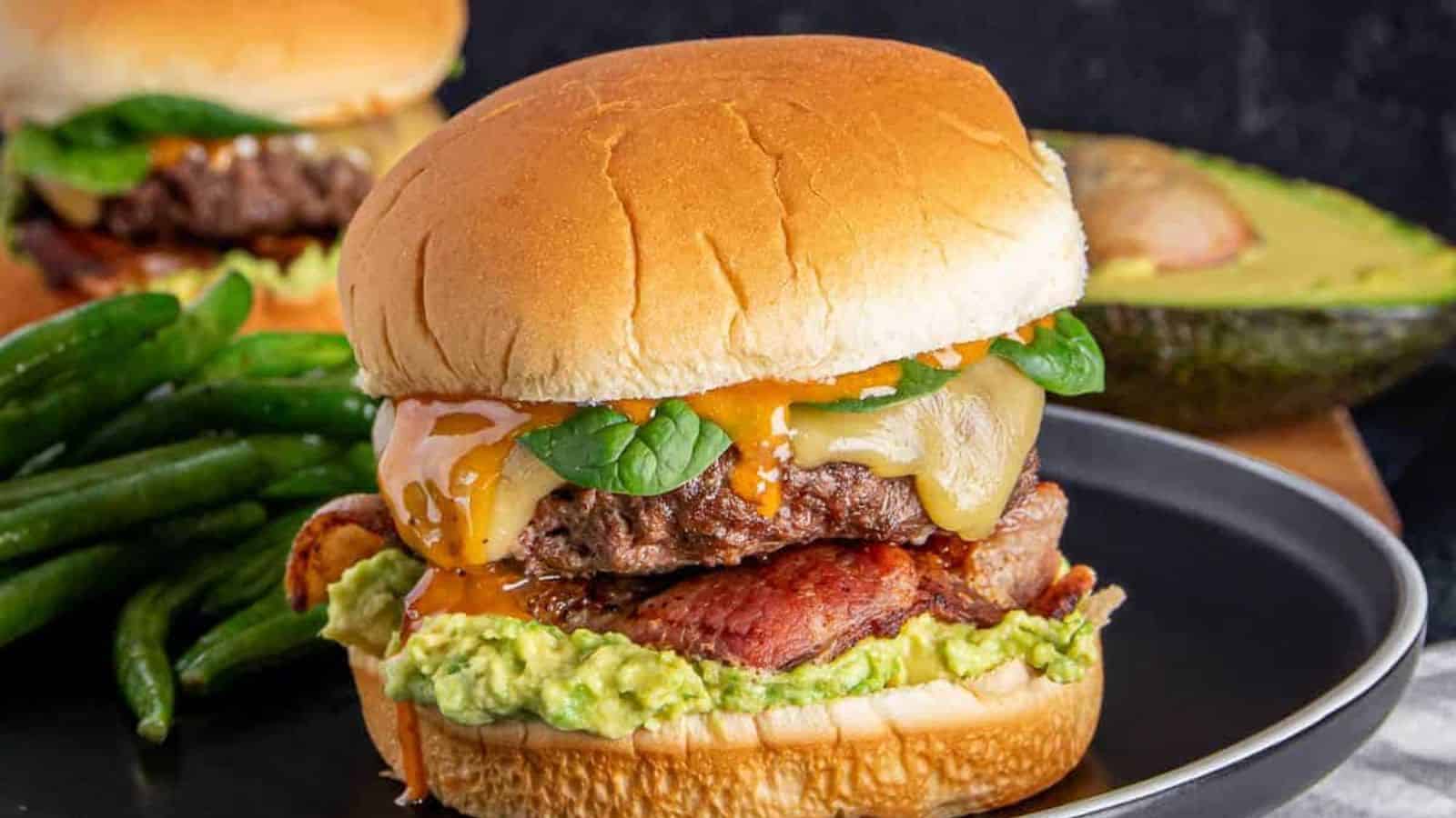 An up-close shot of bacon-avocado ground beef burger on a flat white surface.