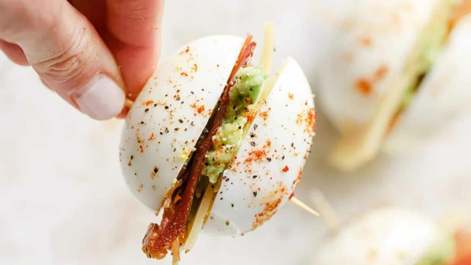 A hand holding a toothpick with a bacon egg and cheese breakfast slider.