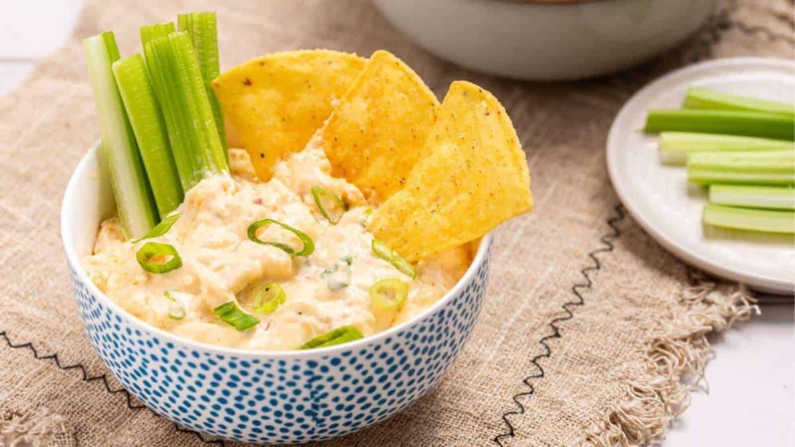 A bowl of buffalo chicken dip with celery and chips.