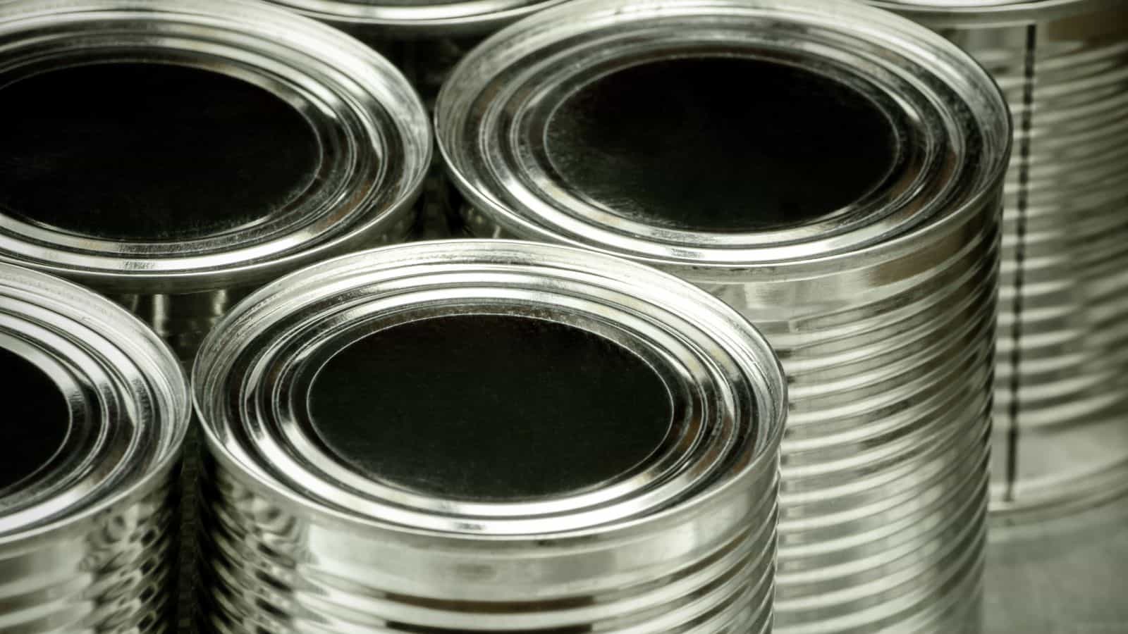 A close-up image of several metal cans with sealed lids. The cans are arranged closely together, showing their smooth, shiny surfaces. They appear to be new and unused, with no labels attached.