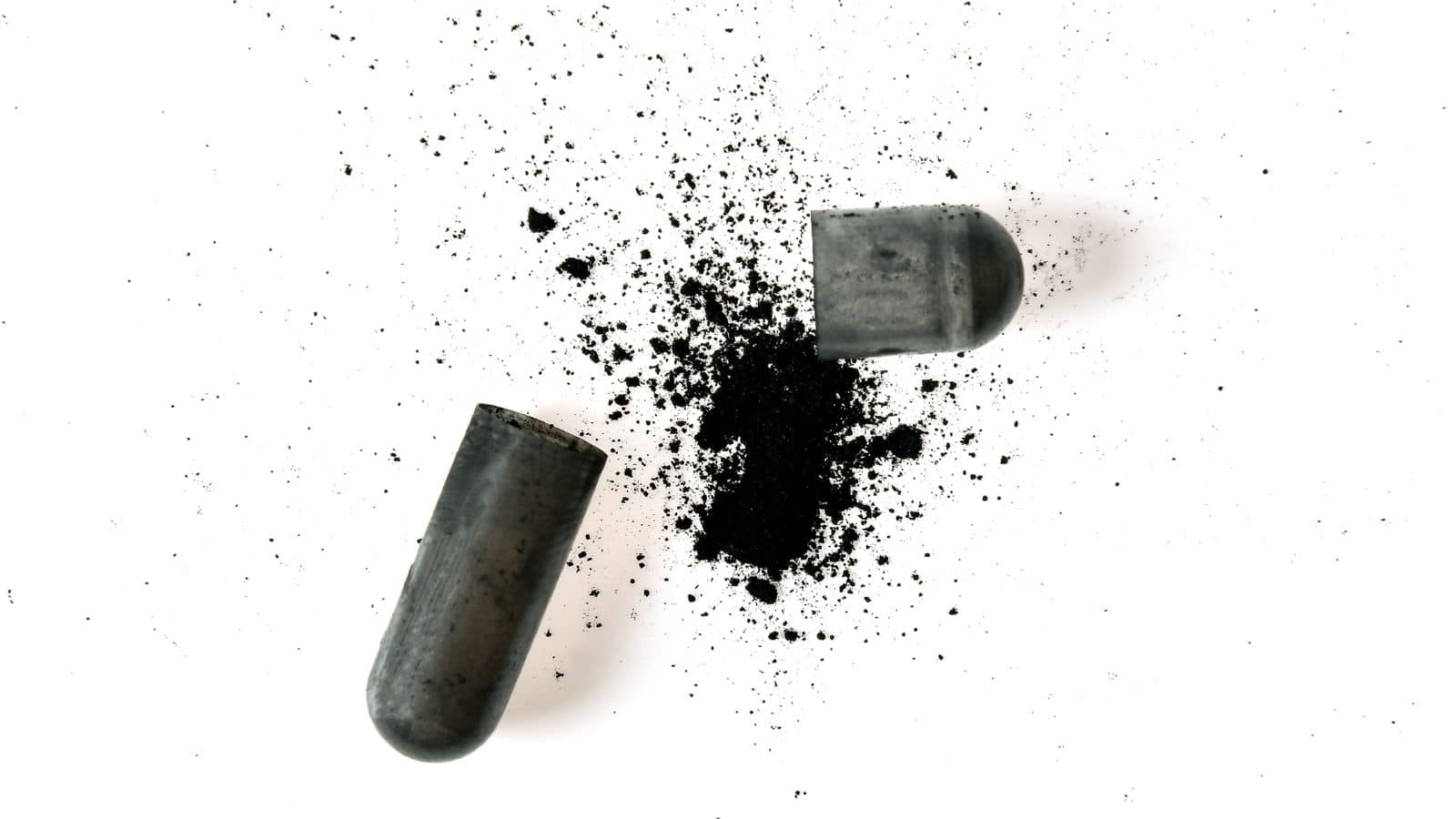 A black capsule is broken in half, spilling its powdered contents onto a white surface. The powder is scattered around both halves of the capsule.