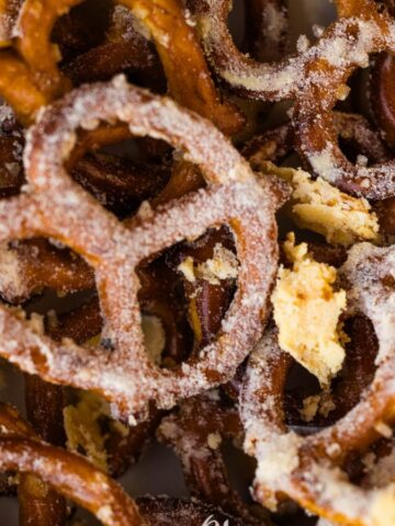 A close-up image of salted pretzels. The pretzels are brown, crunchy, and have visible salt crystals. Some crumbs are scattered among the pretzels.