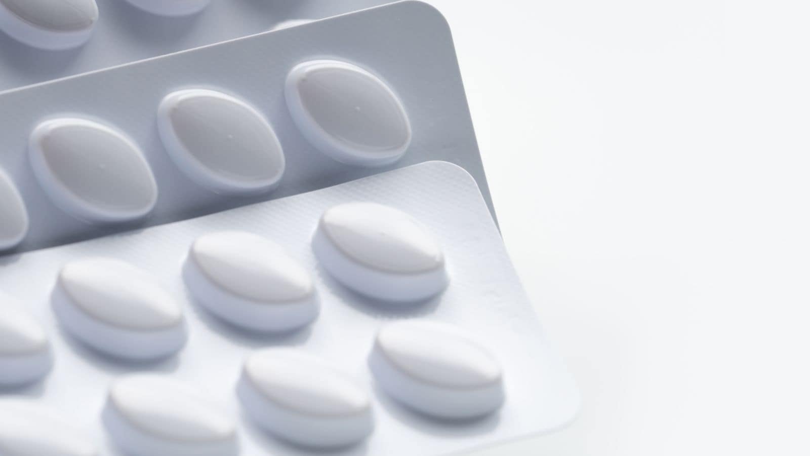 Close-up of three blister packs containing multiple white oval tablets on a white surface. The tablets are evenly spaced inside their individual compartments in the packaging, which is partially overlapping.