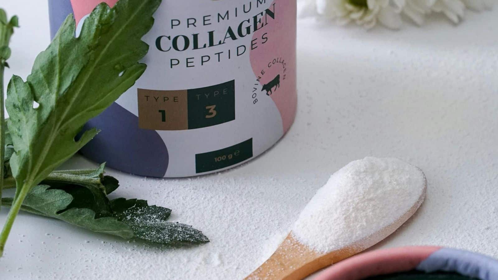A container labeled "Premium Collagen Peptides" with types 1 and 3 indicated sits on a surface. A wooden spoon holds a small amount of white powder next to the container. Nearby are green leaves and a white flower.