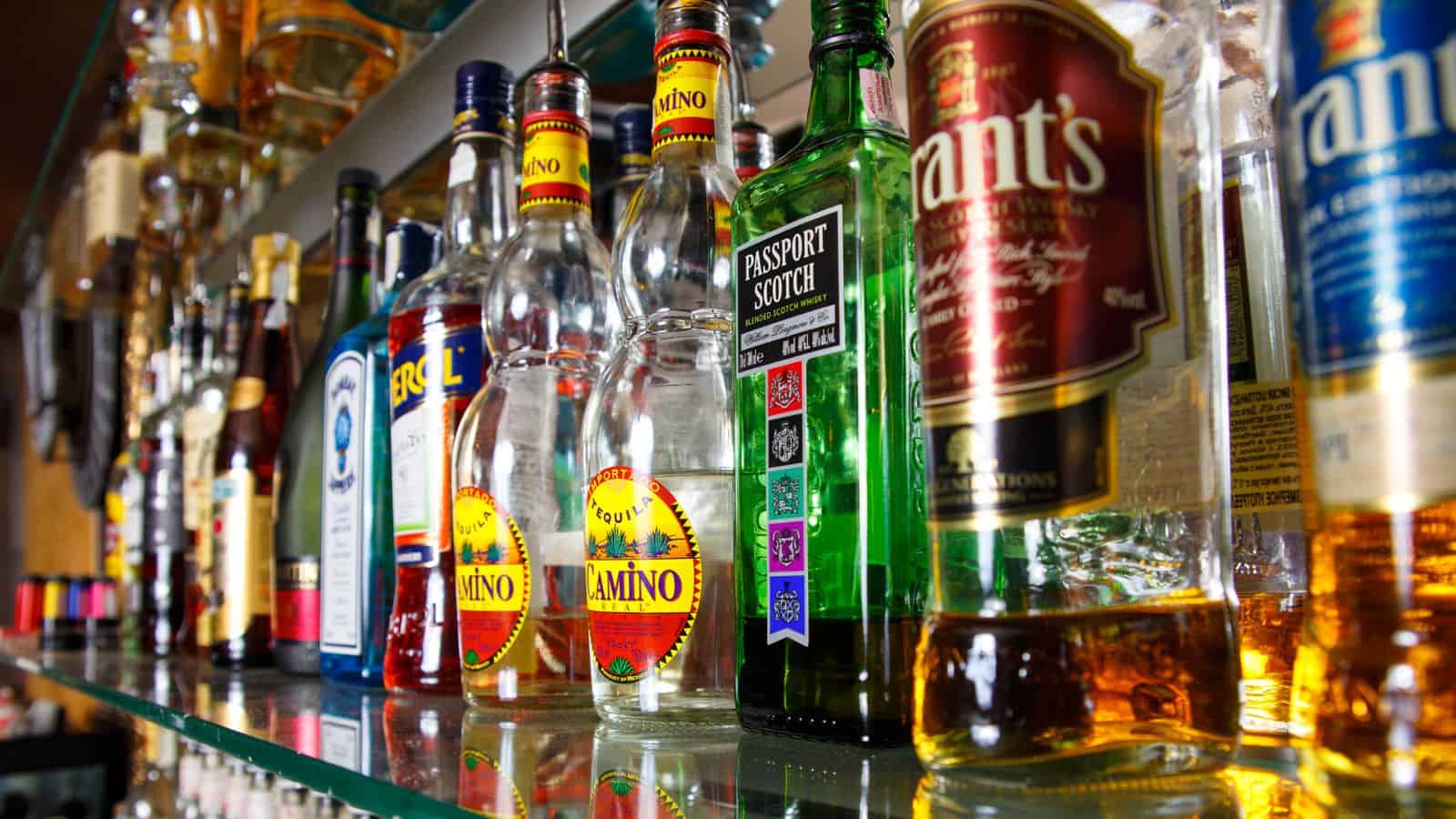 A shelf displaying various liquor bottles, including brands like Passport Scotch and others with colorful labels. The bottles are arranged closely together, showcasing a selection of different alcoholic beverages.