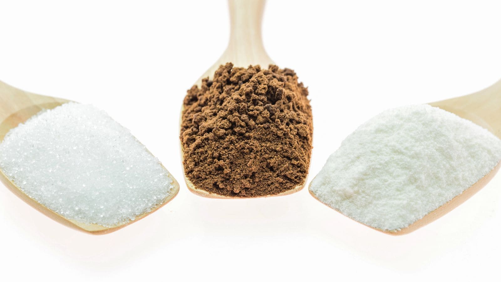 Three wooden spoons each hold a different substance: granulated white sugar on the left, finely ground brown powder in the center, and fine white powder on the right, all set against a white background.