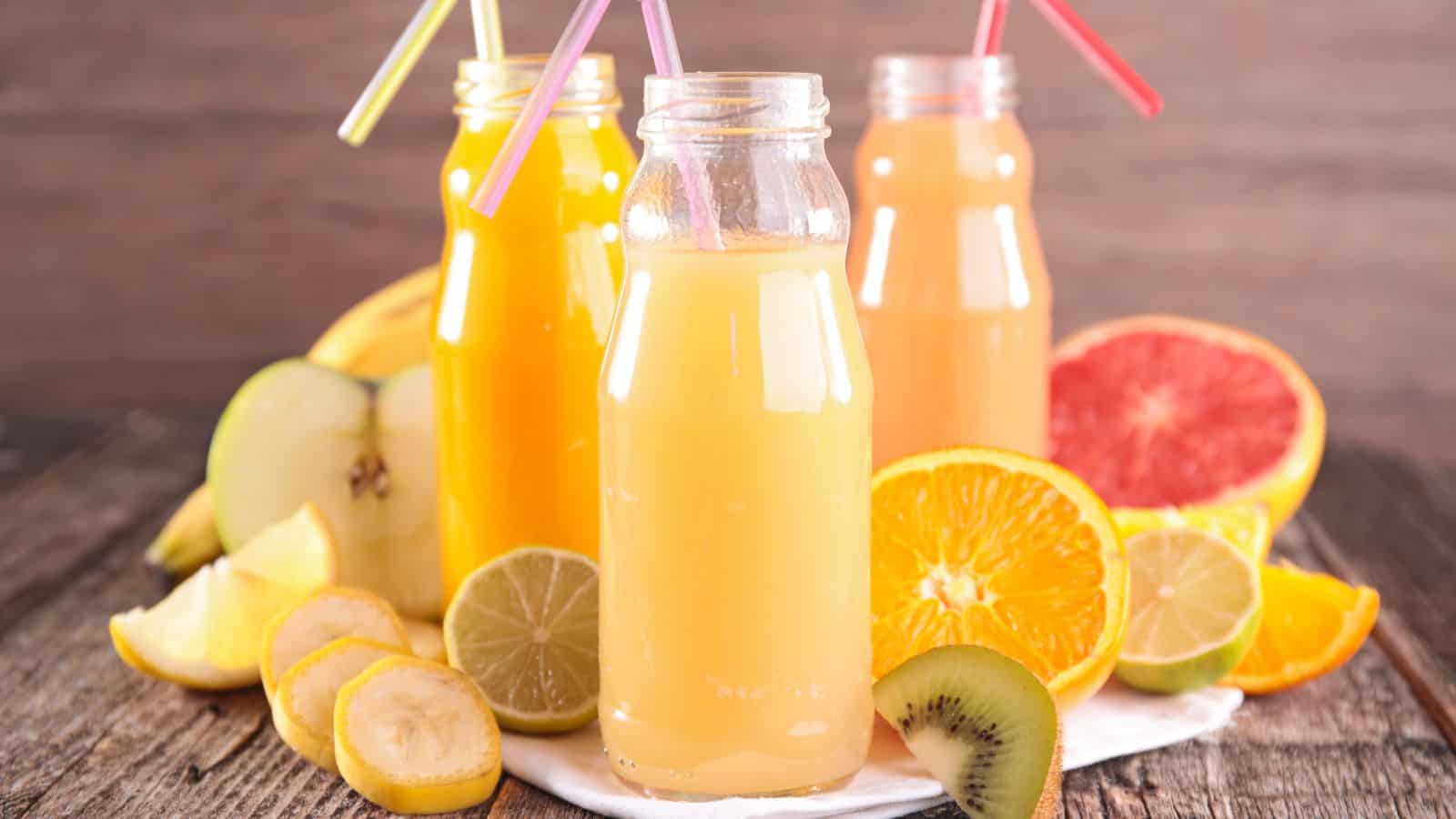 Three glasses of fruit juices with fruits at the sides.