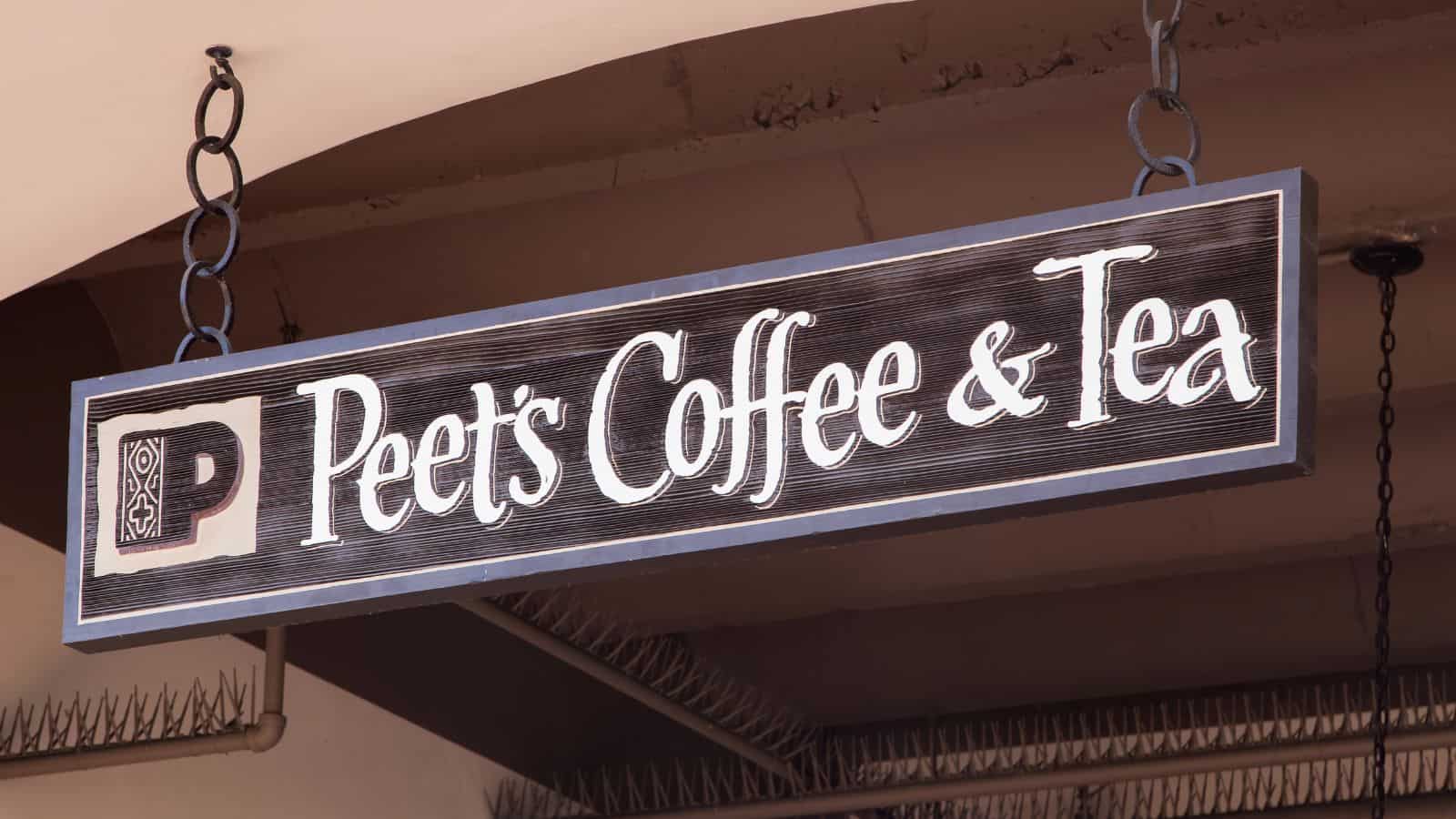 A hanging sign reads "Peet's Coffee & Tea" with a decorative "P" logo on the left side. The sign is under a ceiling and is supported by chains. The background shows part of a building structure.