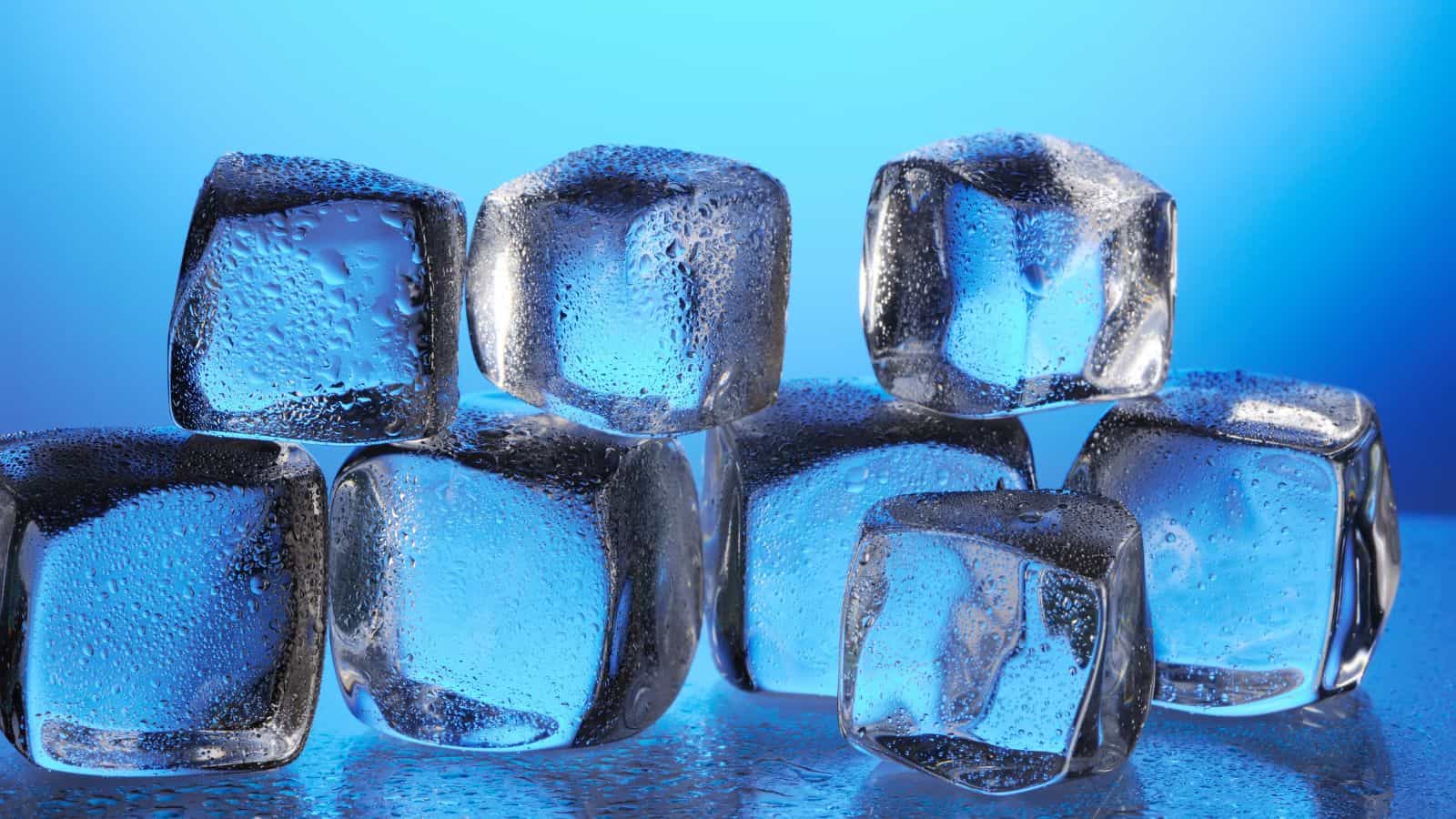 A close-up of several ice cubes stacked on top of each other against a blue background. The ice cubes have visible water droplets and are illuminated, giving them a clear, glossy appearance.