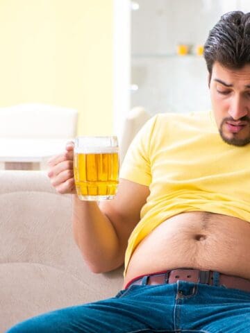 A man holding a beer and looking at his belly.