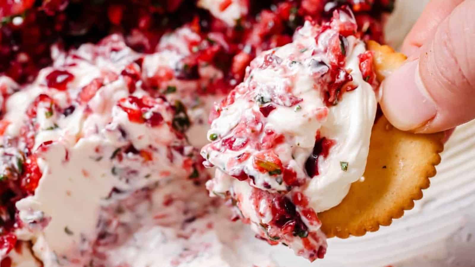 A cracker being dipped into a dish of jalape&ntilde;o cranberry dip.