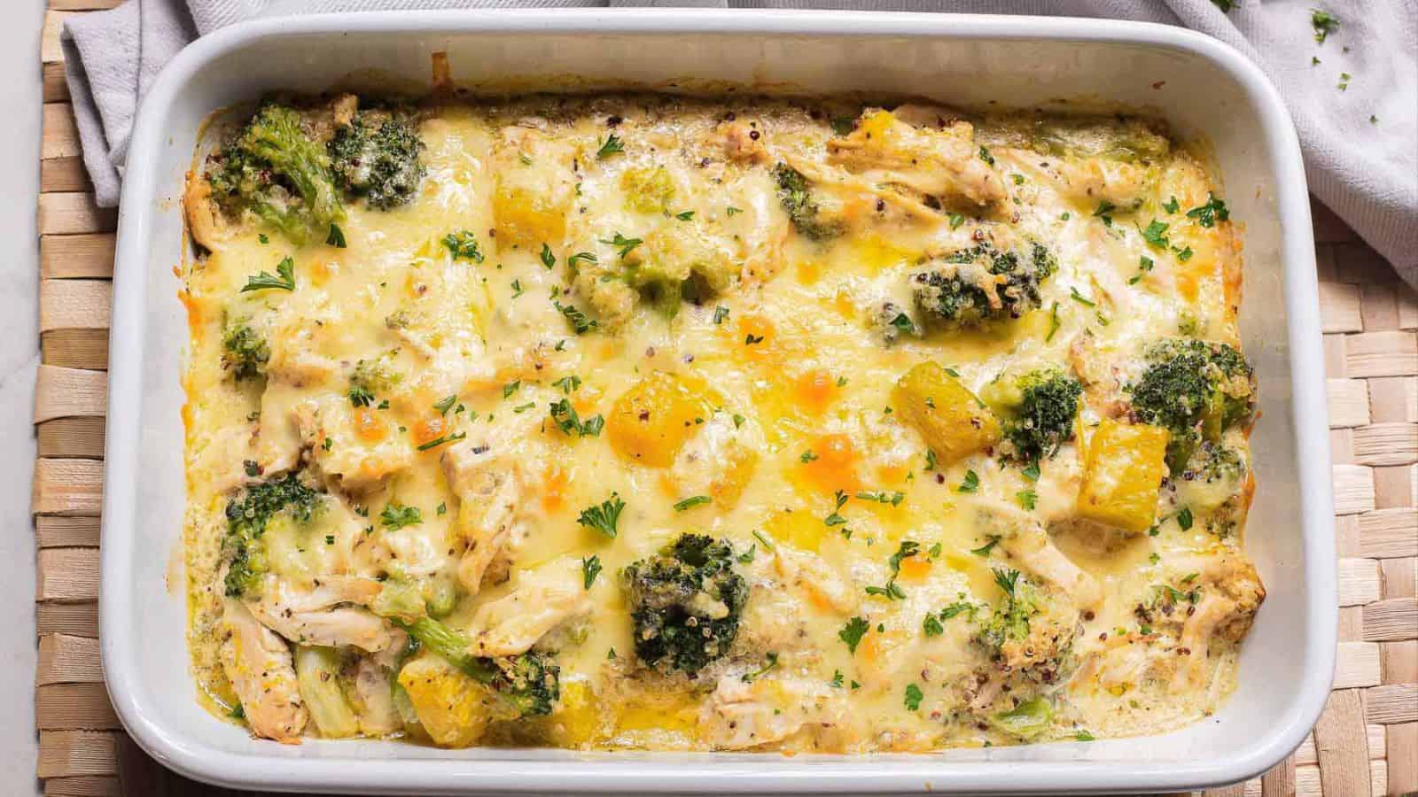 A baked casserole dish containing a cheesy broccoli and chicken mixture, topped with pieces of pineapple and sprinkled with chopped parsley.