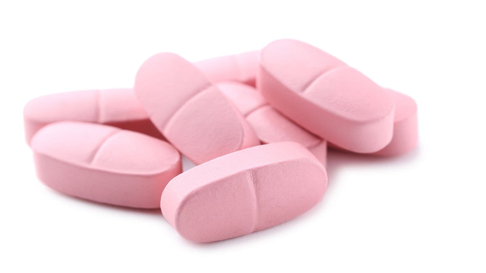 A group of pink, oval-shaped tablets, some with a scored line down the middle, are scattered on a white background.