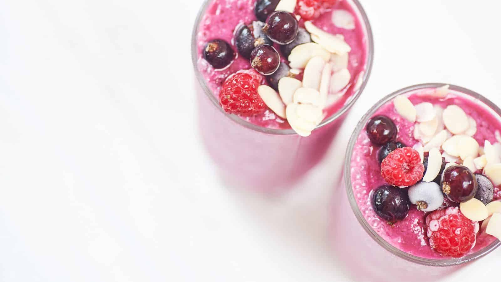 Two glasses of fruit smoothies with fruit and nut toppings.